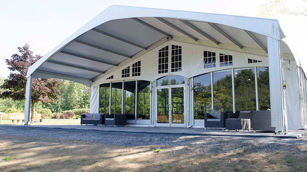 Clearspan Structure Tent Rental — Glass Walls and Covered Porch Clearspan structure tent with curved roof, glass walls, french doors, and covered porch with lounge seating