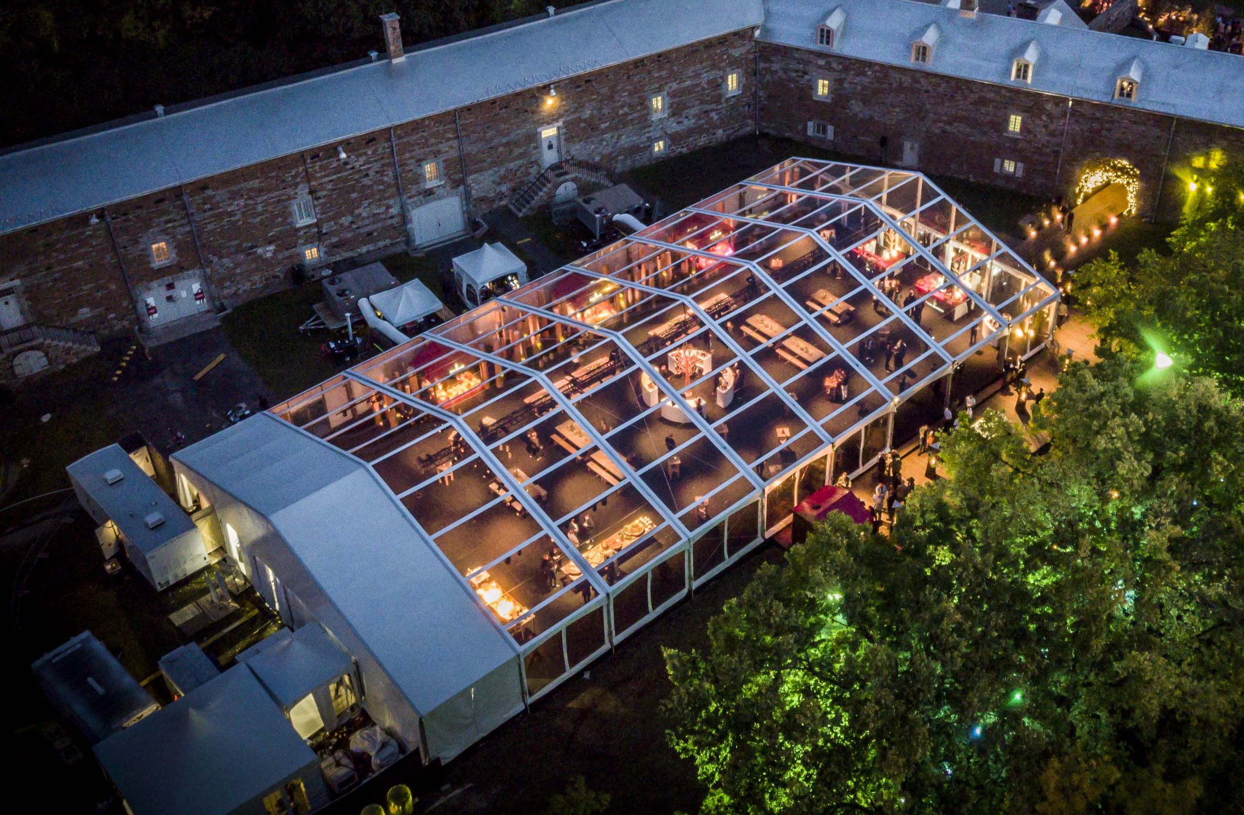Clear-top event structure tent illuminated at night in courtyard setting for entertainment and corporate events