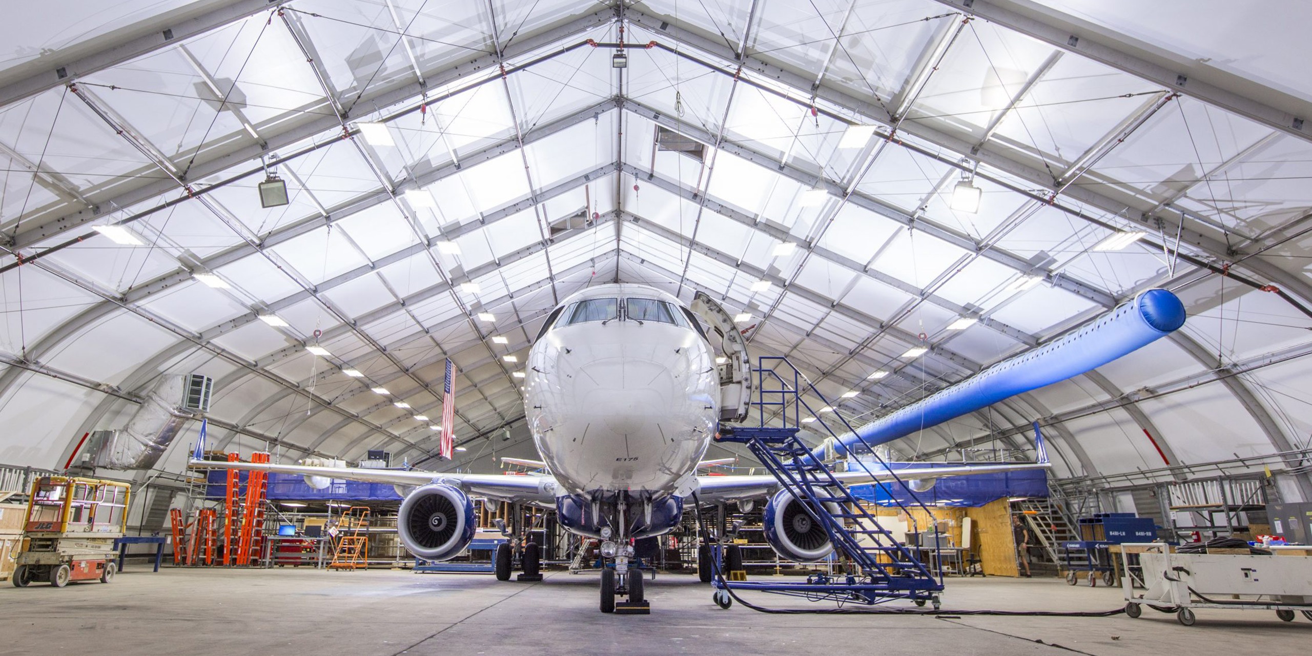 Aircraft Hangar Structure — Commercial Airplane Maintenance Interior of clearspan aviation hangar structure with commercial aircraft undergoing maintenance and work platforms alongside fuselage