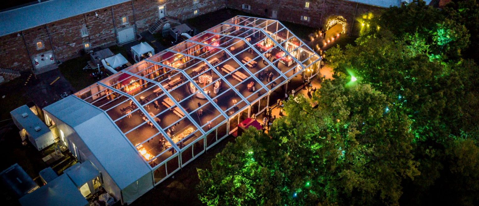 Aerial view of clear-top wedding structure tent at night with warm ambient lighting and elegant table settings