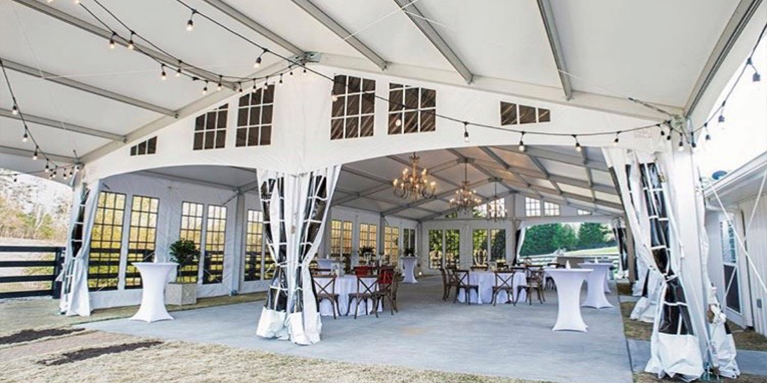 Elegant wedding and event structure interior with chandeliers, drapery, bistro lighting, and banquet table setup for private dining