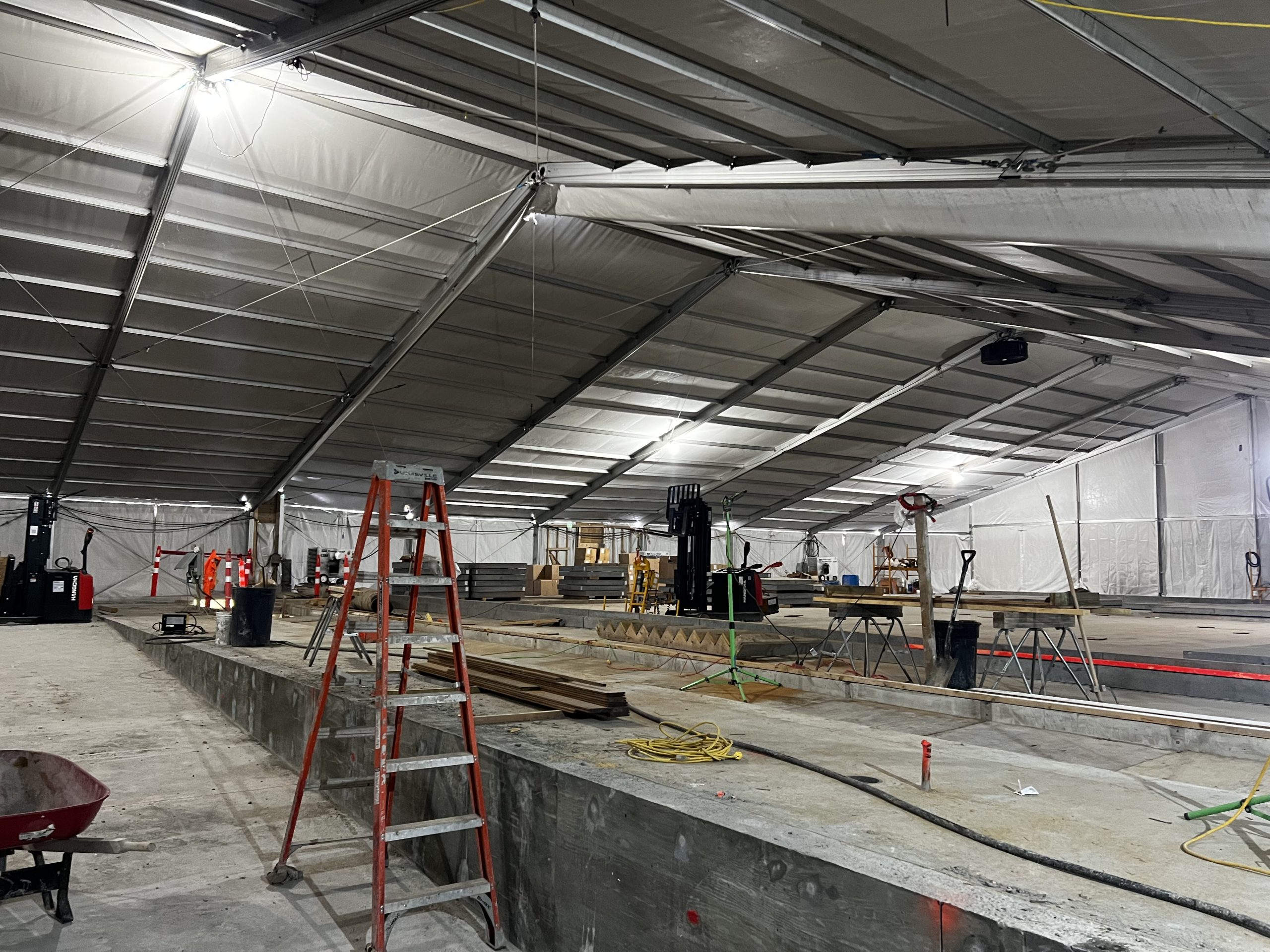 Interior of heated construction tent with concrete forms, ladders, and work equipment for concrete curing operations