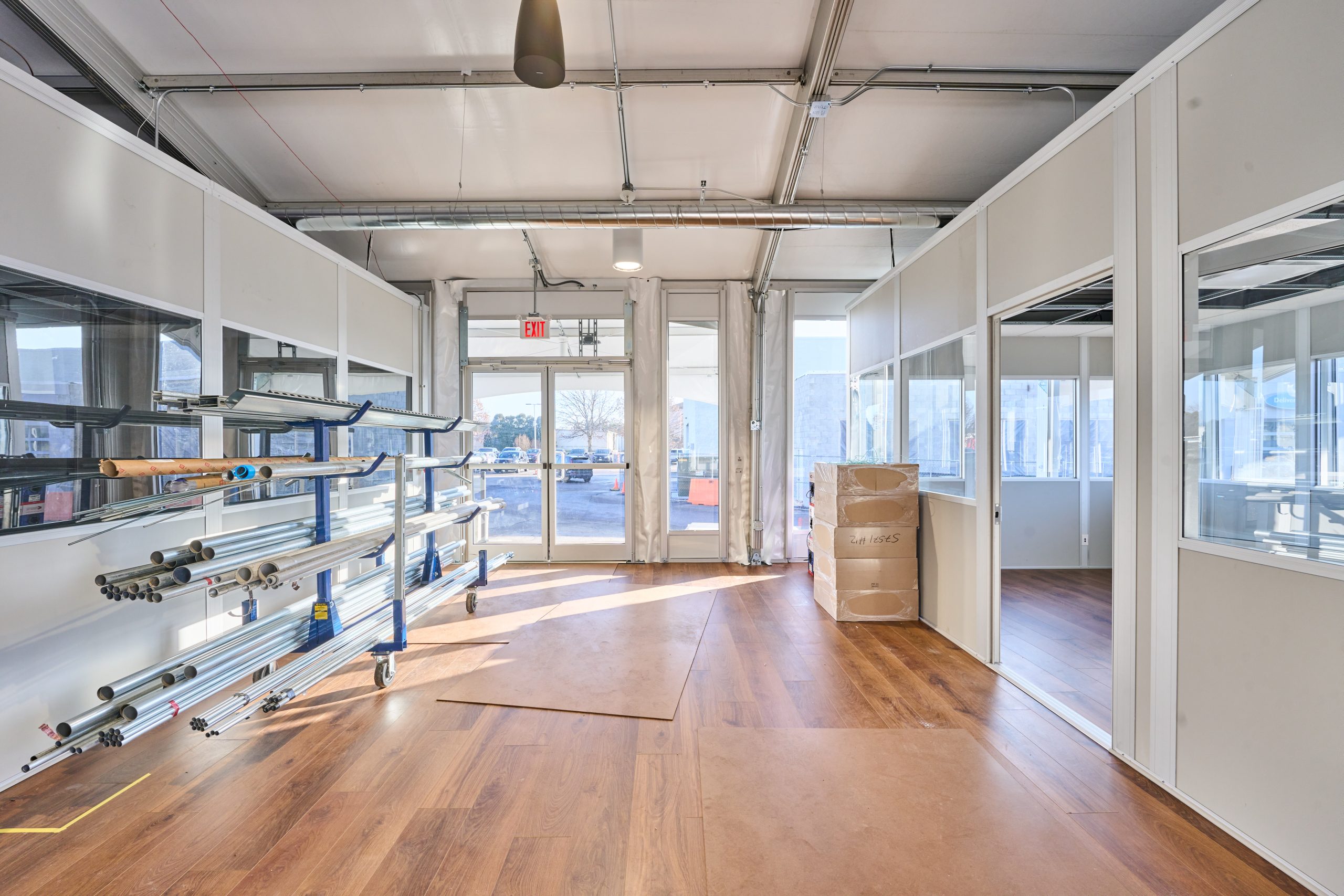 Interior of temporary structure with hardwood flooring, glass partitions, aluminum frame overhead, and natural light from glass walls